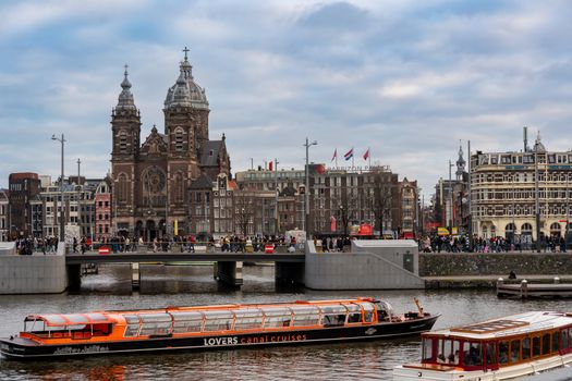 Scenic view of the Basilica of Saint Nicholas alongside Amsterdam's canal, featuring a tour boat.