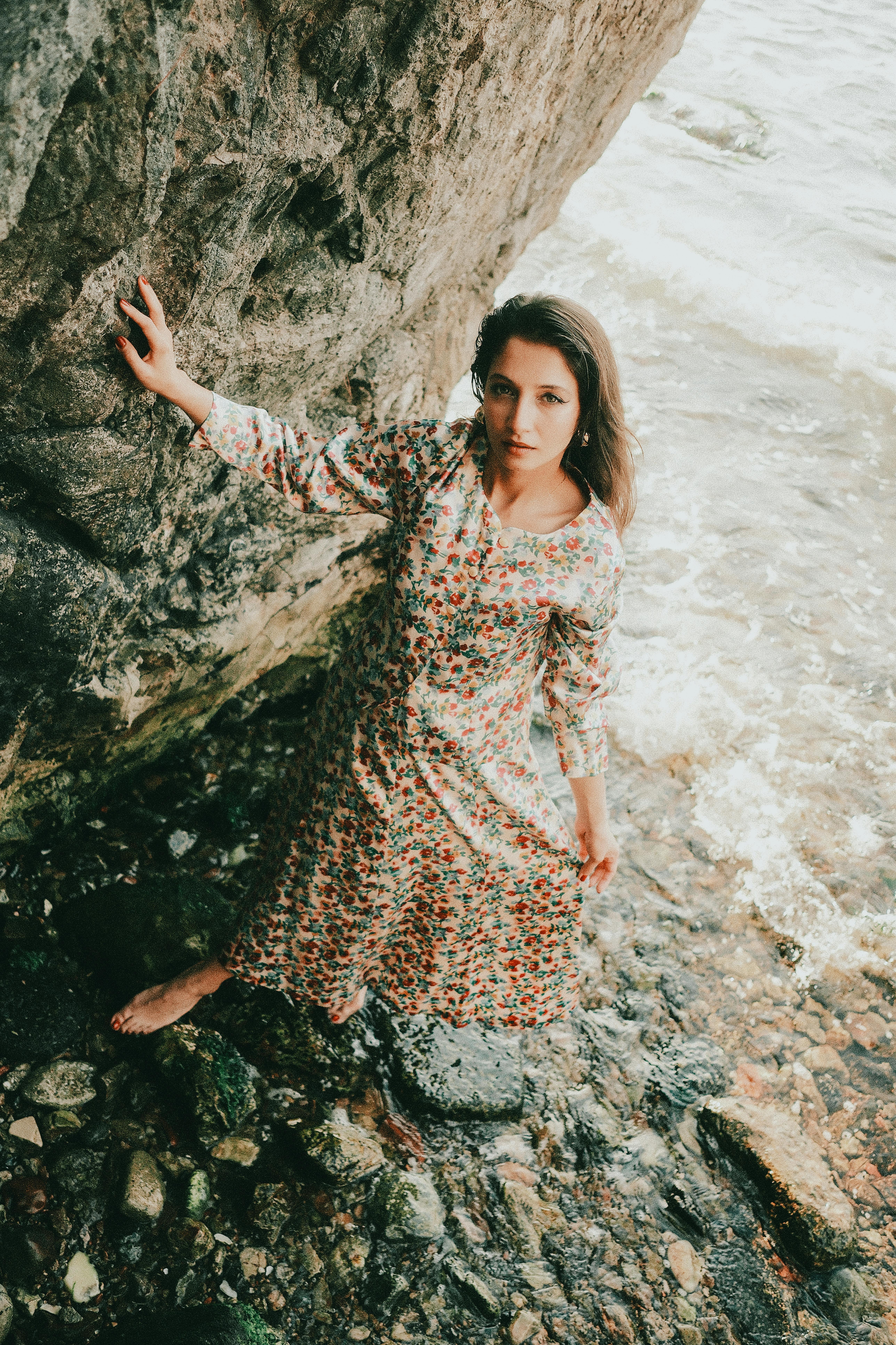 身着花裙的女人站在岩石海边，散发着优雅和自然之美
