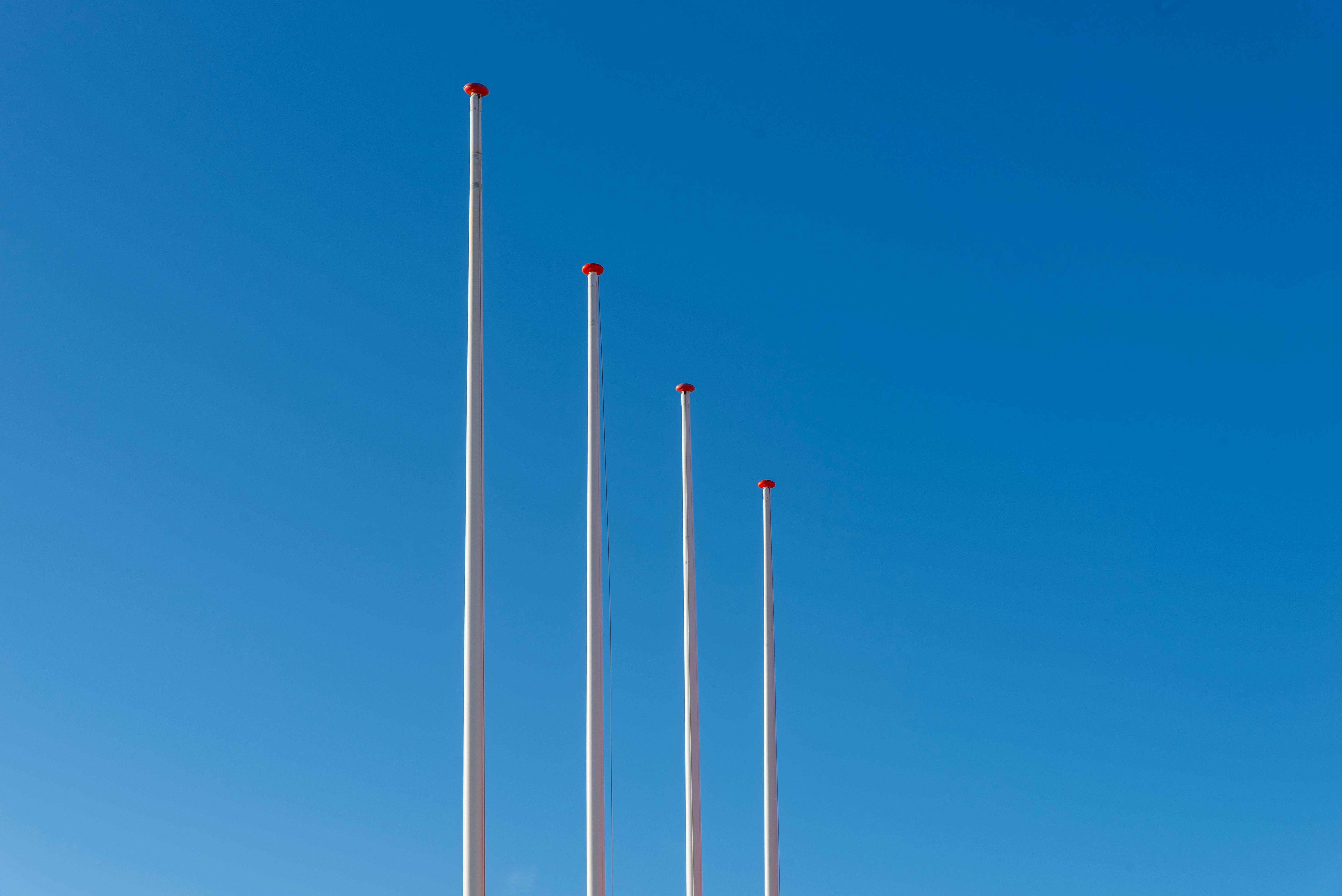 Gratis Fire symmetriske flaggstenger reiser seg mot en klar blå himmel og fremhever minimalistisk design og utendørs atmosfære. Arkivbilde