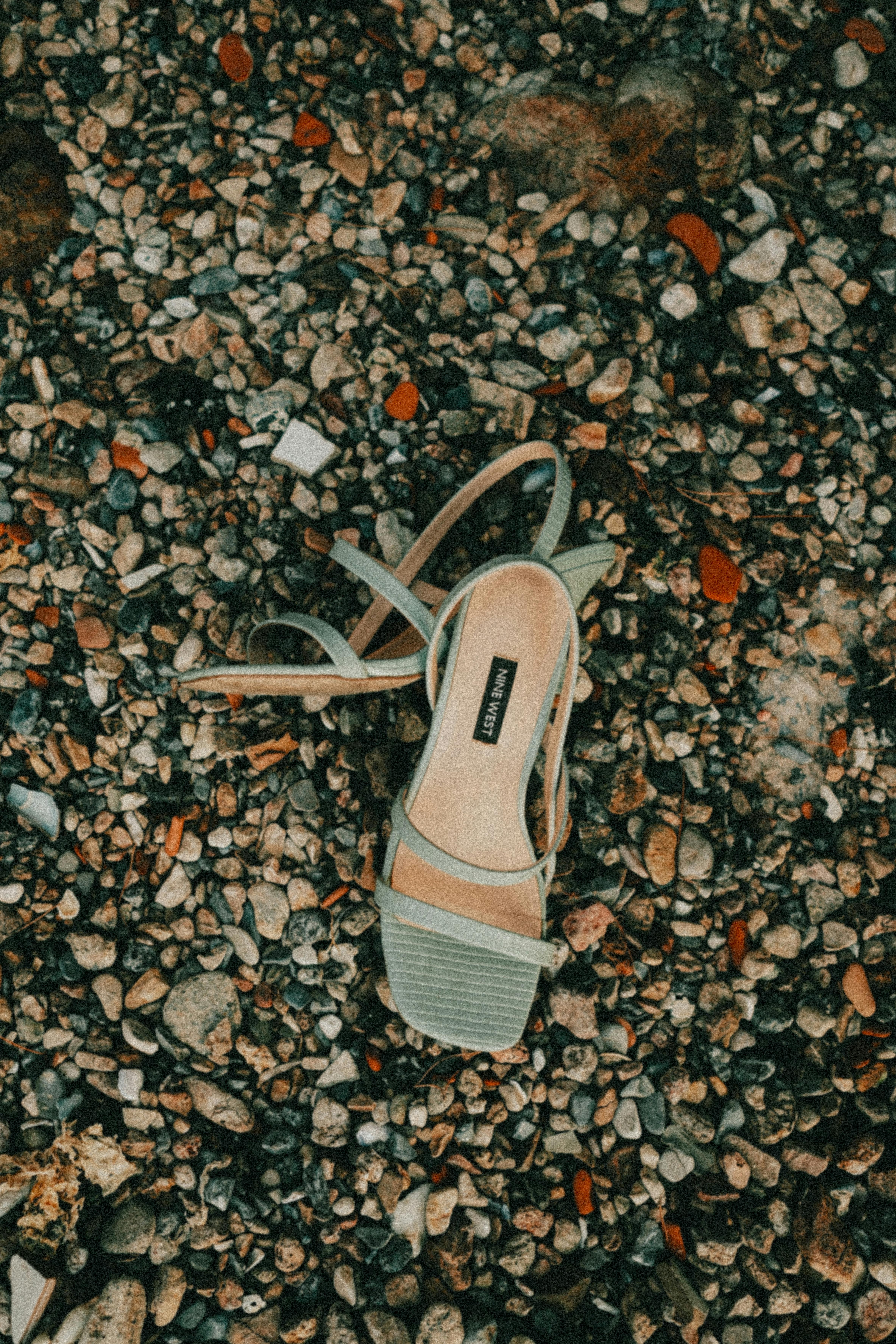 Kostenlos Künstlerisches Foto einer Riemchensandale an einem Kieselstrand, das Textur und Farbkontrast hervorhebt. Stock-Foto