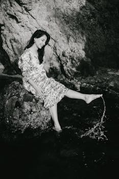 Serene portrait of a woman sitting on rocks by the sea in black and white.