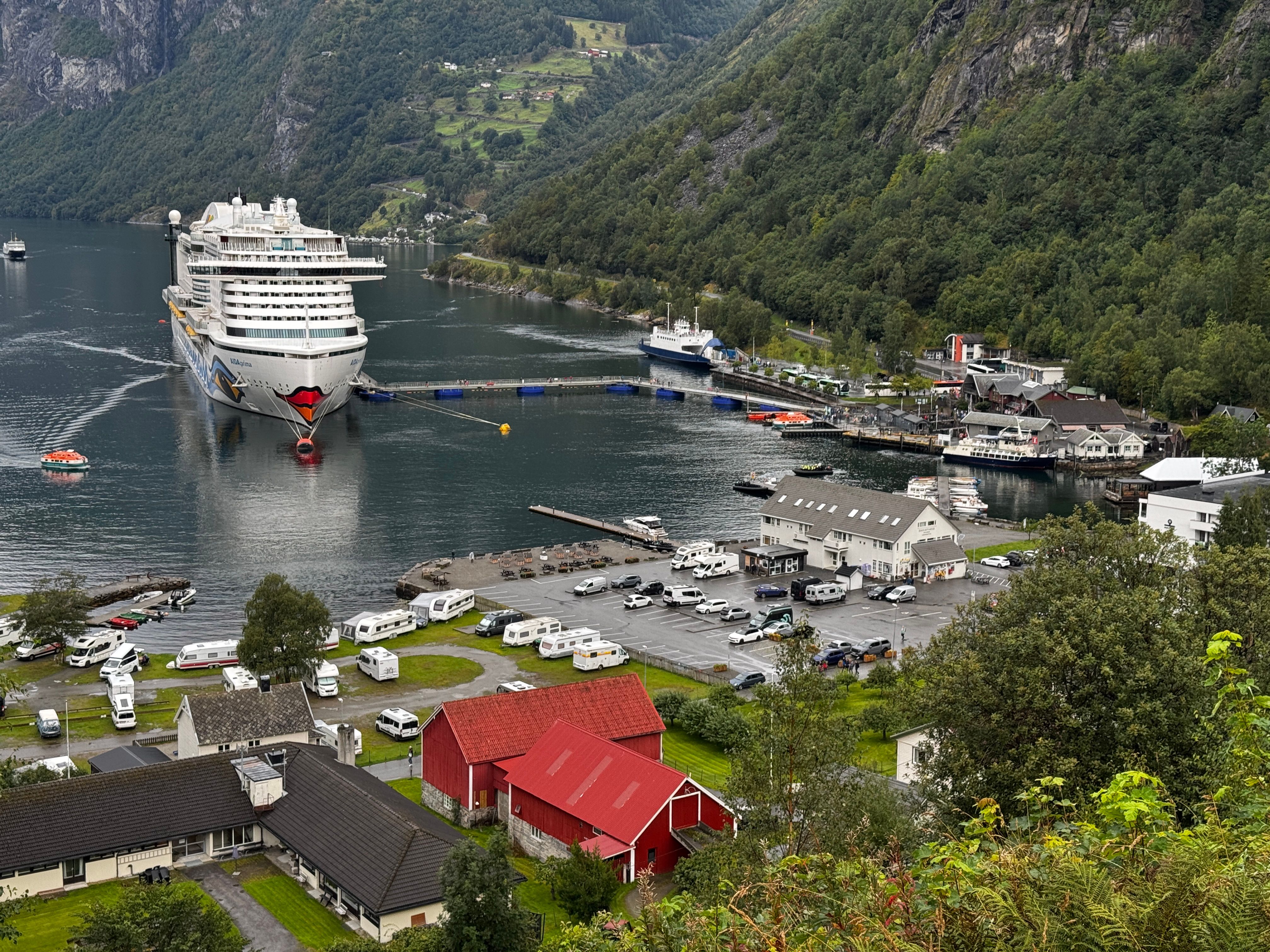 A large cruise ship docked in Geiranger, Norway, surrounded by mountains and lush greenery.