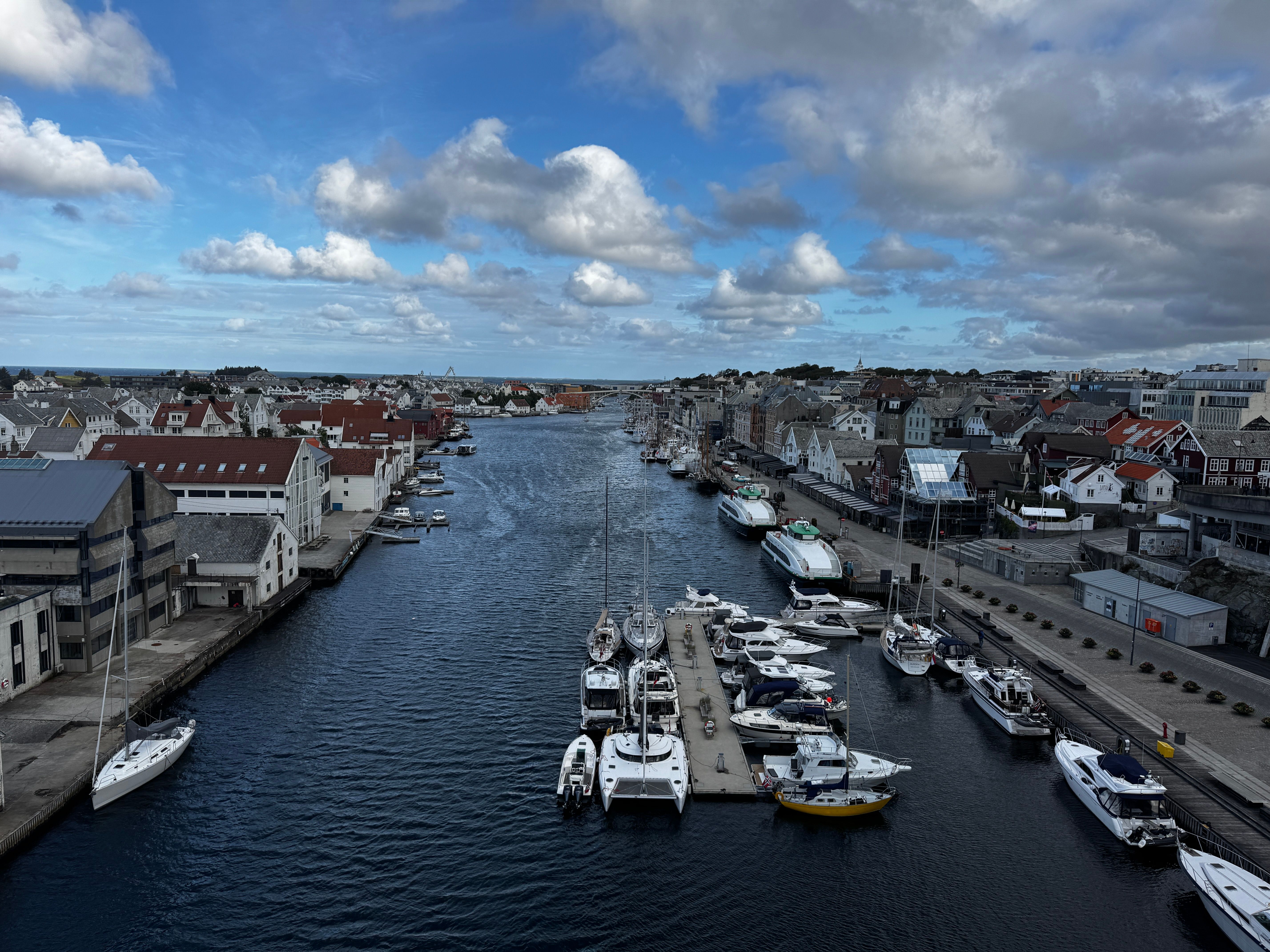 A scenic view of Haugesund harbor with moored boats, quaint buildings, and a vibrant sky.