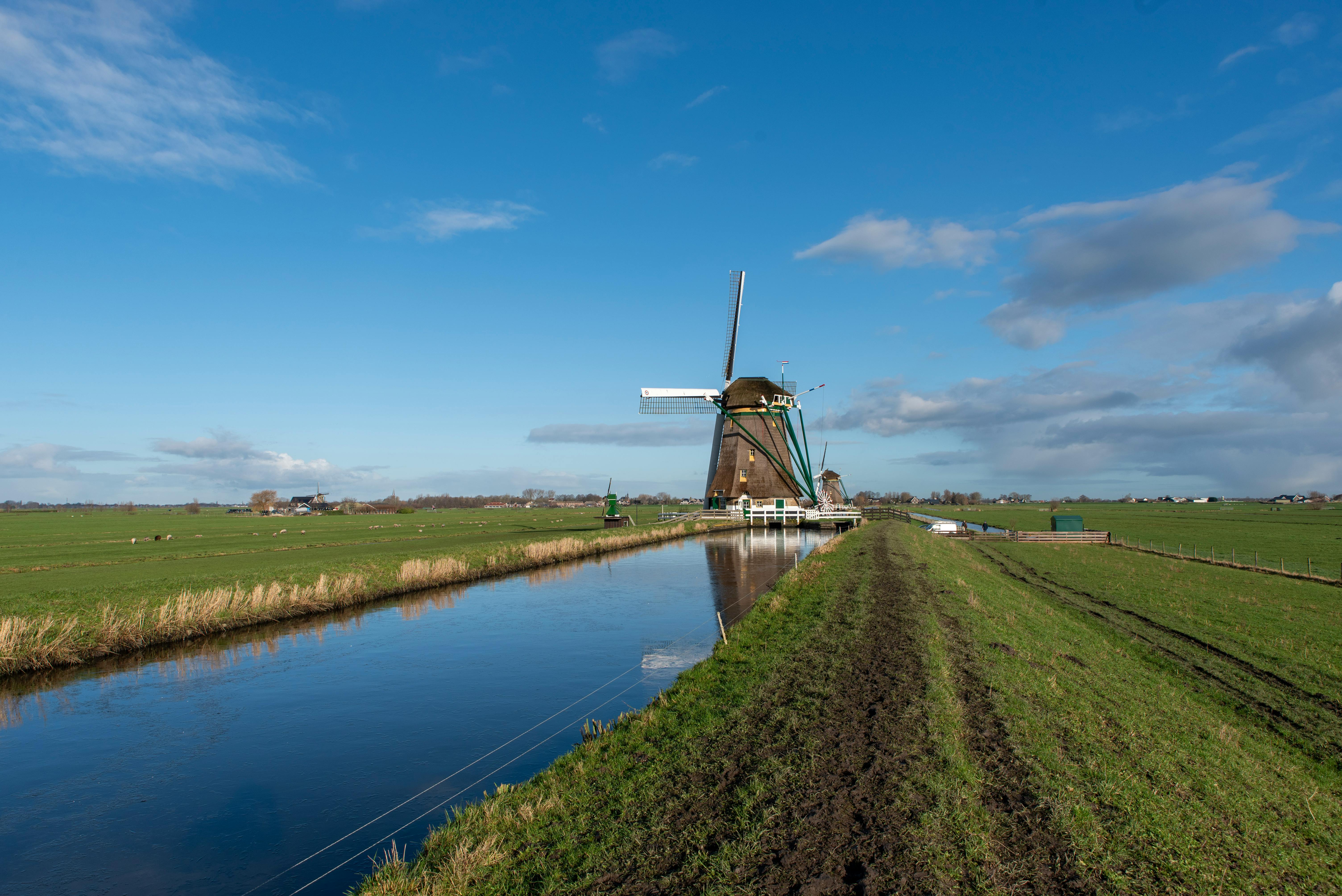 Scenic view of a historic windmill by a canal in Aarlanderveen, Holland, under a blue sky.
