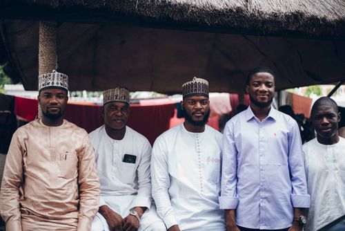 Free Five men posing outdoors wearing traditional and casual attire under a thatched roof. Stock Photo