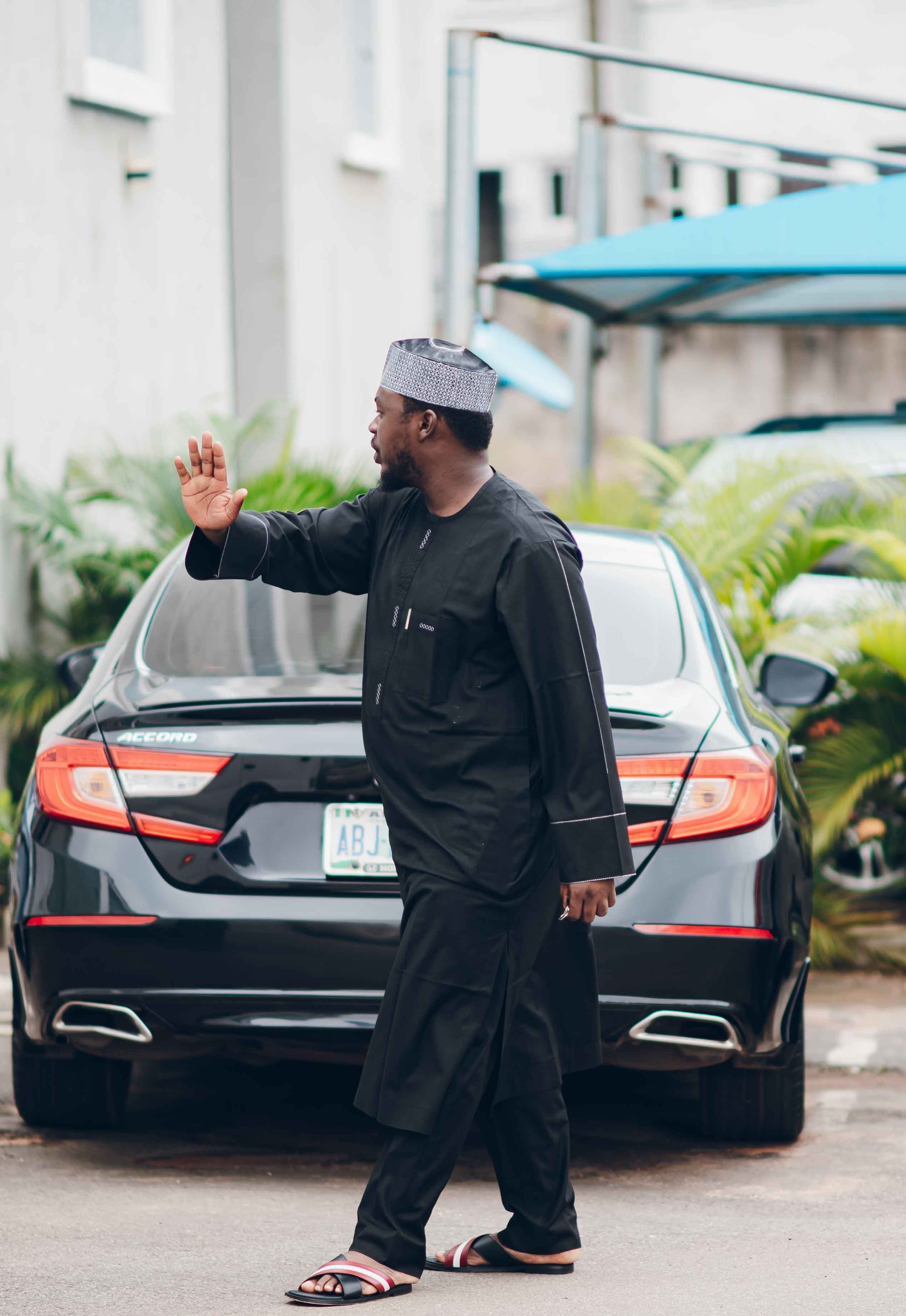 Man in black traditional attire walking by a car, daytime shot.