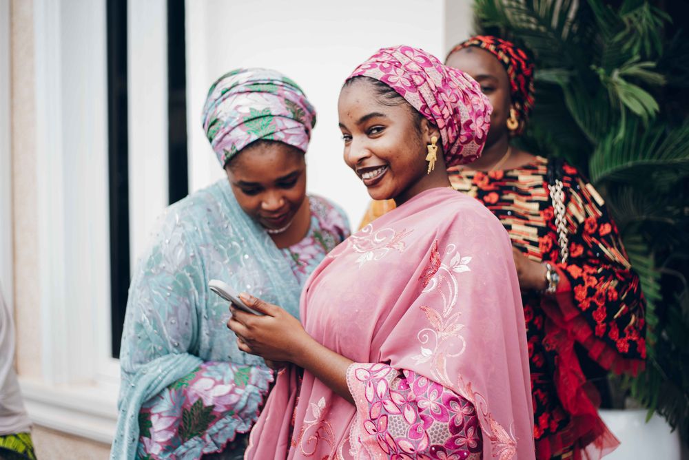Friends in colourful traditional attire laughing over a phone together