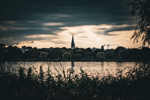Free St. Nikolai Church spire silhouetted against a dramatic sunset by Alster Lake in Hamburg. Stock Photo