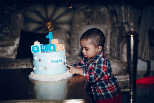Adorable toddler enjoying first birthday with colorful cake indoors.