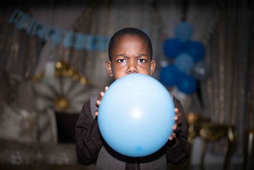 A child inflates a blue balloon during an indoor birthday celebration.