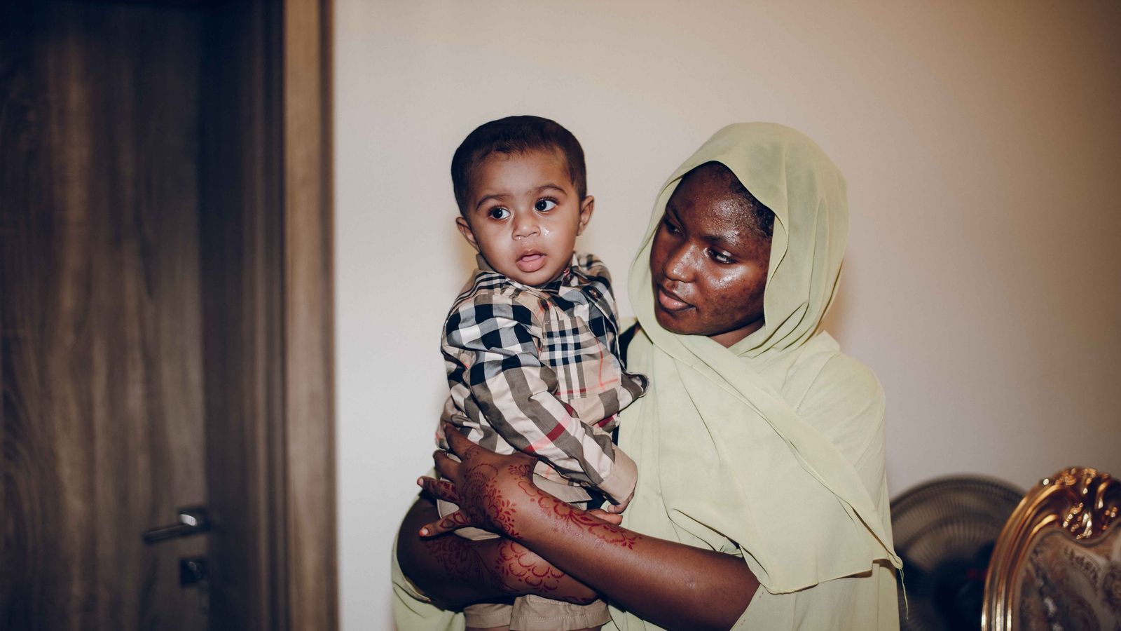 A mother lovingly holds her baby while indoors, showcasing their cultural attire.