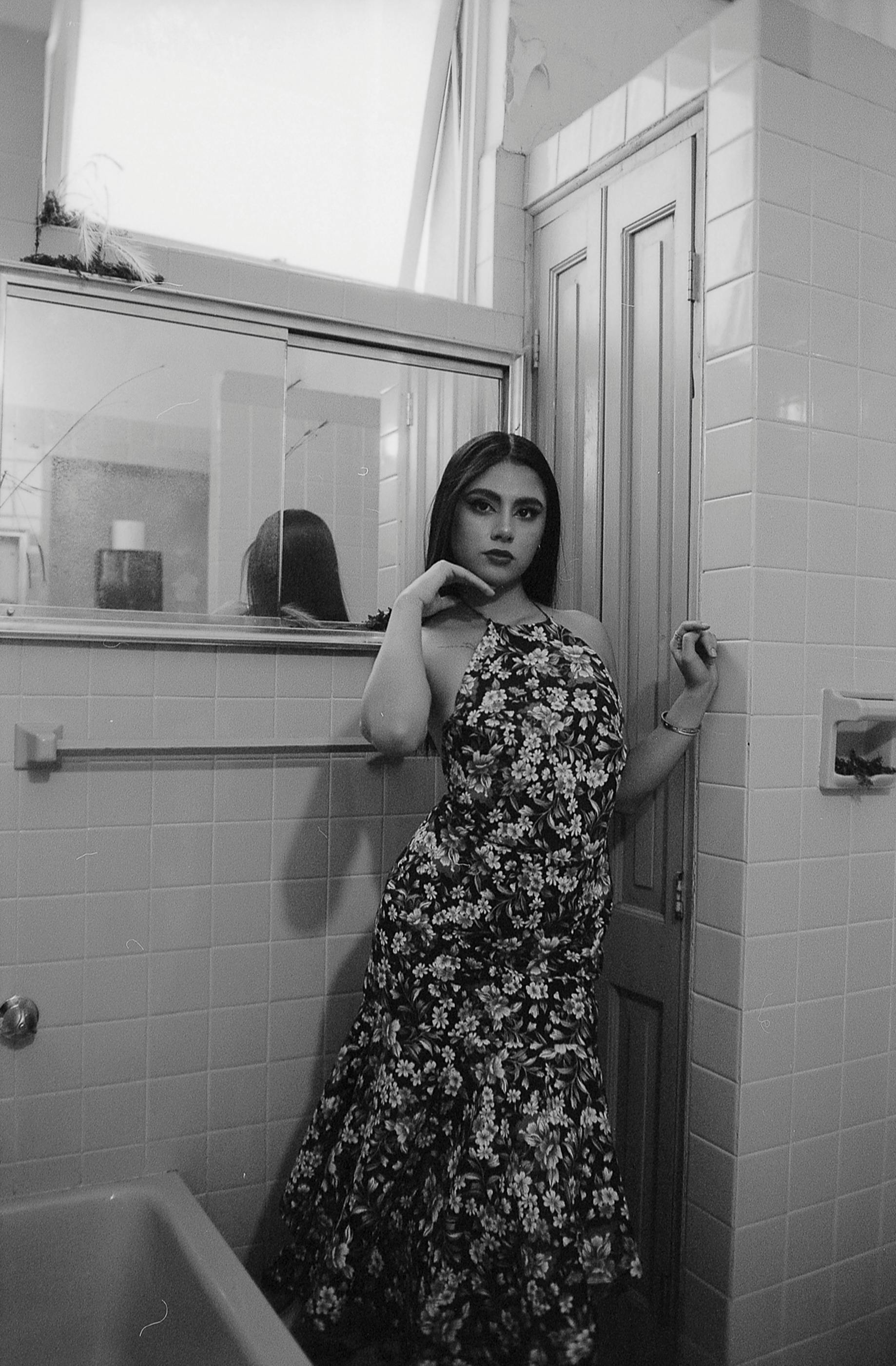 Gratis Ritratto in bianco e nero di una donna con un abito floreale in posa in un bagno piastrellato. Foto a disposizione