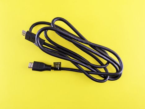 A neatly coiled black HDMI cable displayed on a vibrant yellow surface, ideal for tech visuals.
