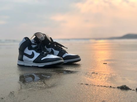 Black and white sneakers on a sandy beach reflecting golden sunset light.