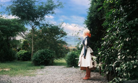 A woman in cosplay attire standing among greenery in a vibrant garden setting.