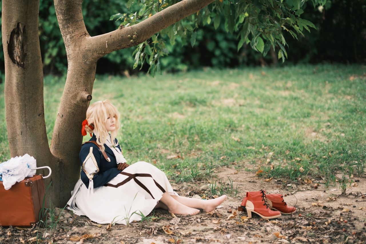 cosplayer in white dress resting under a tree in a serene outdoor sett