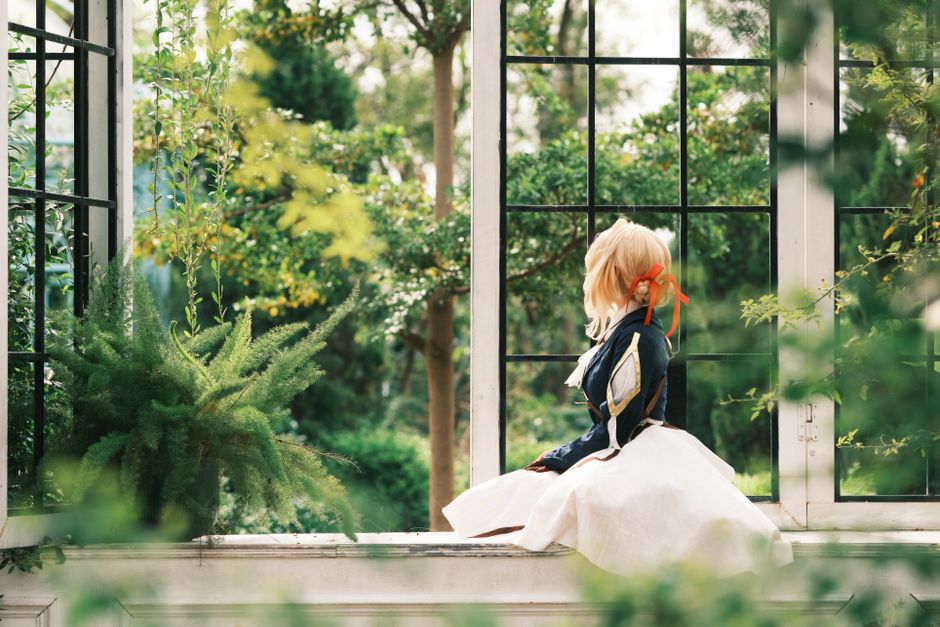 A cosplayer in a garden setting, seated by a window, surrounded by lush greenery.