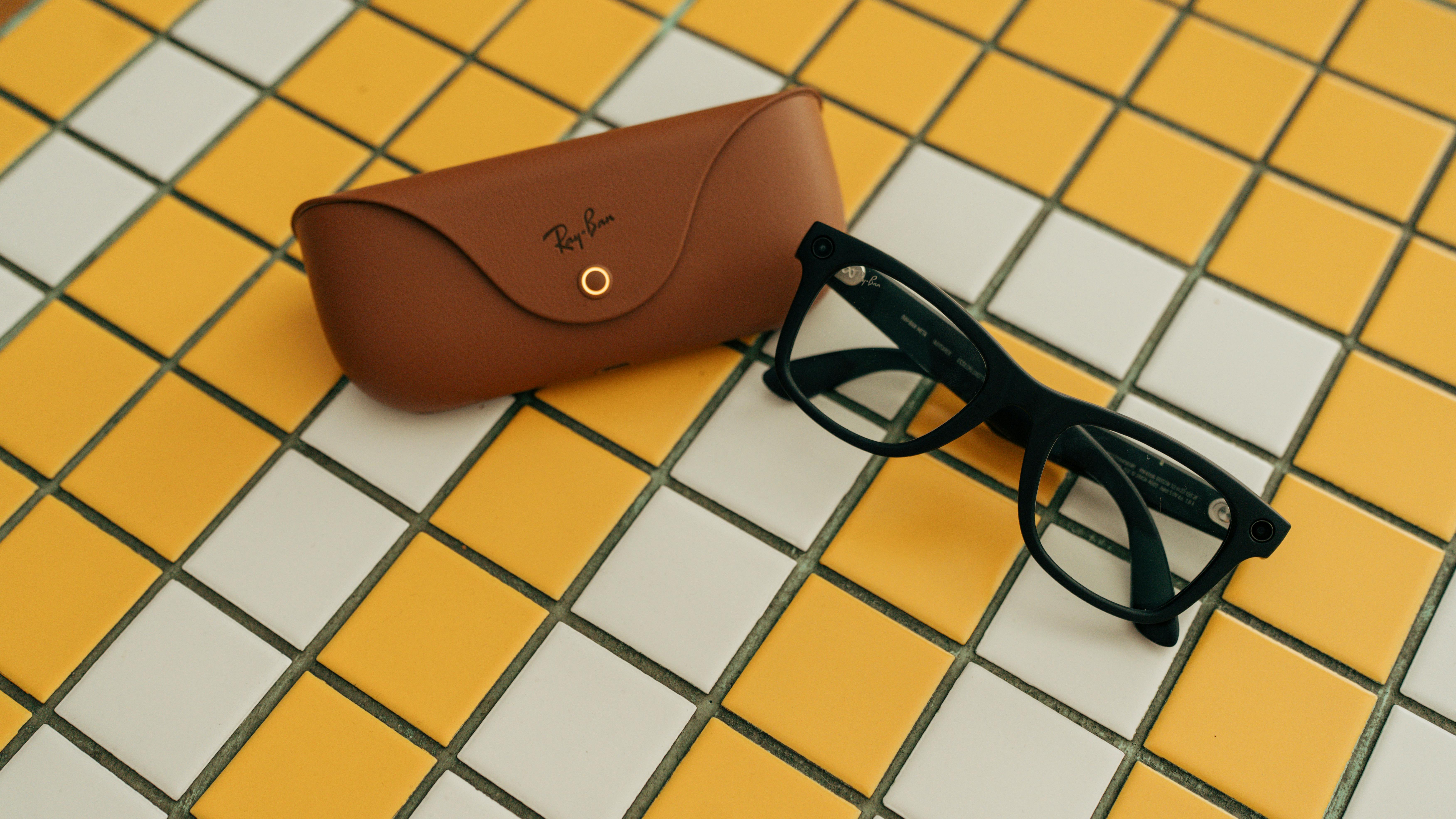 Kostenlos Schwarze Brille mit braunem Etui auf gelb-weiß gefliestem Hintergrund. Stock-Foto