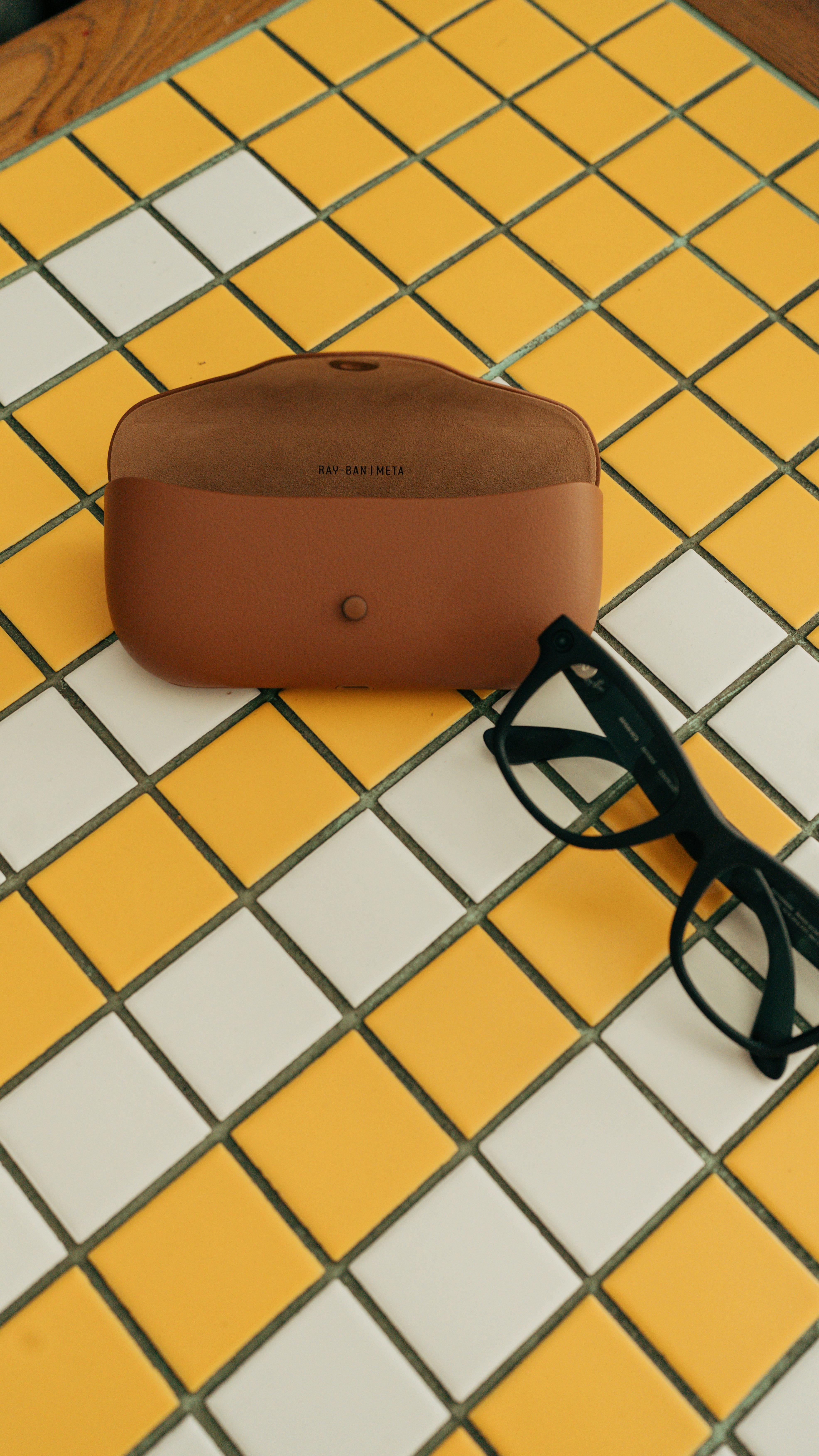 Free Black sunglasses and a brown leather case on a yellow and white checkered table surface. Stock Photo