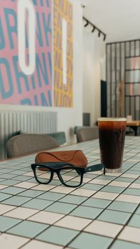Modern café scene with tiled table, iced coffee, and glasses, perfect for lifestyle and design themes.