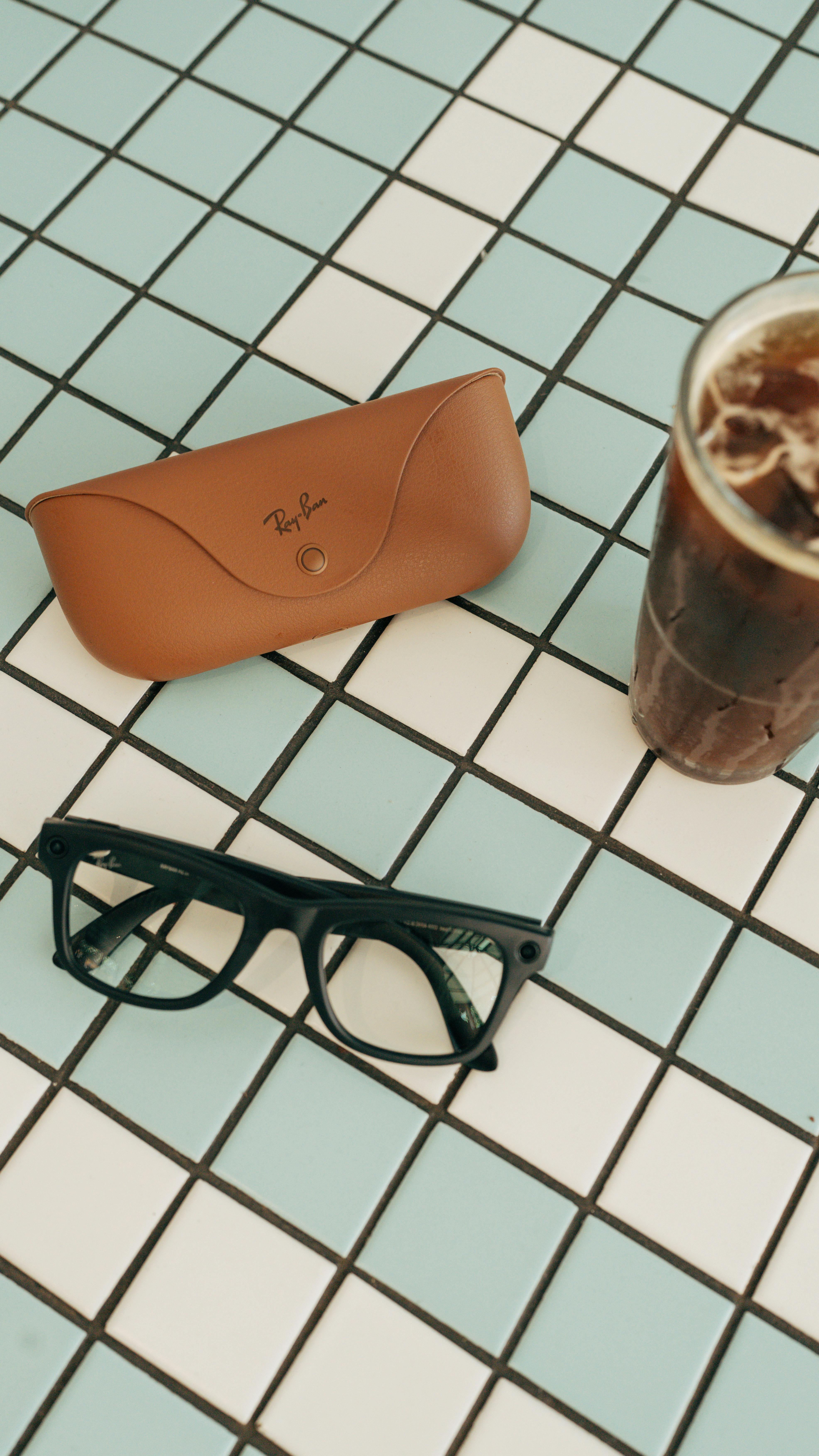 grátis Óculos pretos, estojo de couro e café gelado sobre uma mesa de azulejos azuis. Foto profissional