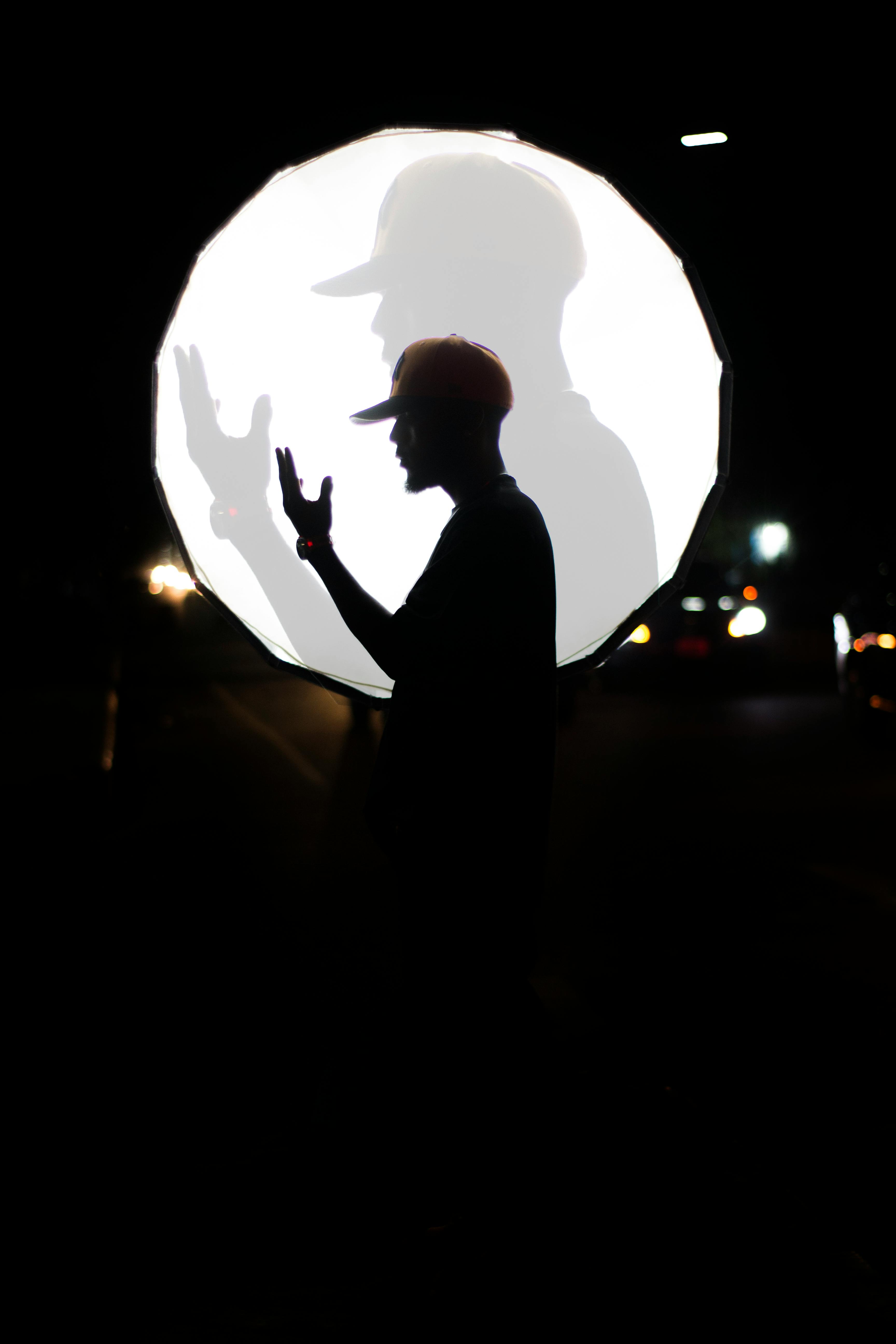 Ücretsiz Gece parlak dairesel bir ışığın önünde şapkalı bir adamın silüeti. Stok Fotoğraflar