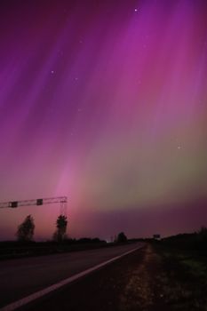 Vibrant aurora borealis lights up the night sky over a peaceful road scene.