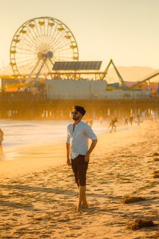 Man strolling on Santa Monica Beach with the iconic pier and Ferris wheel in the background.