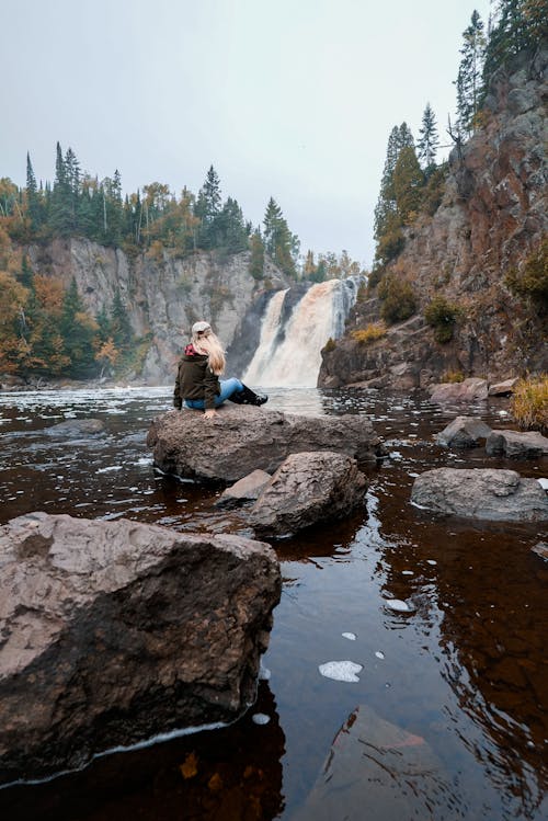 Femme Assise Sur Un Rocher En Face De Chutes D'eau