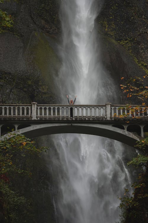 流れる滝の前の橋の真ん中に立っている人