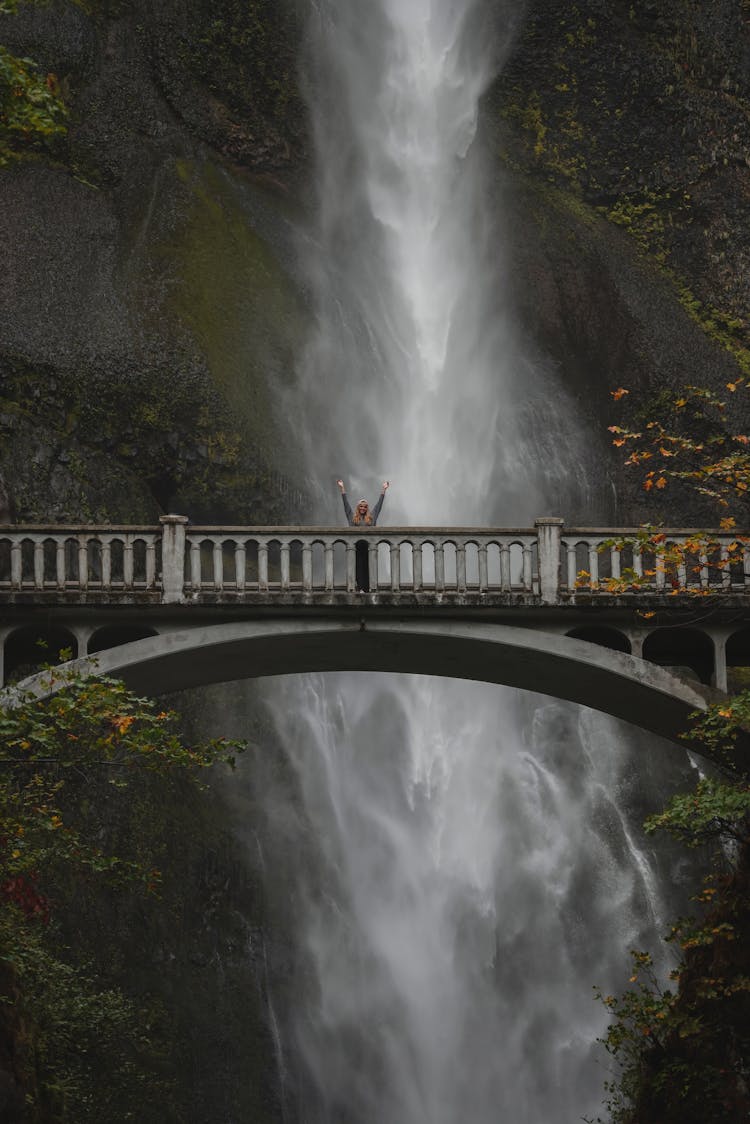 Person Standing In The Middle Of Bridge In Front Of Flowing Waterfall