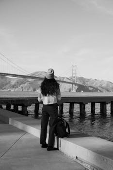 Rear view of a woman observing the iconic Golden Gate Bridge from a waterfront location.