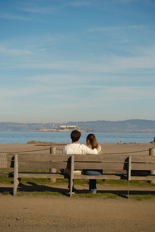 Free Couple sitting on a bench, embracing, overlooking a sunny Los Angeles beach. Stock Photo