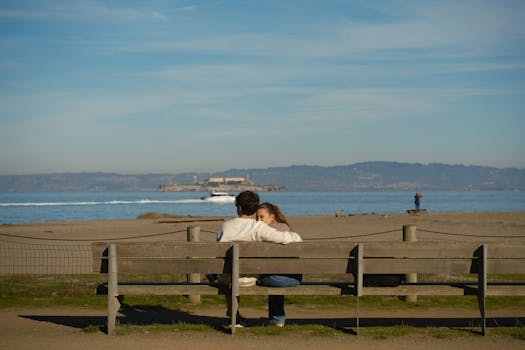 A romantic couple enjoys a serene moment on a beachfront bench with an ocean view in Los Angeles.