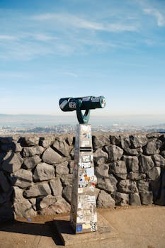 Public telescope with stickers overlooking Los Angeles skyline.