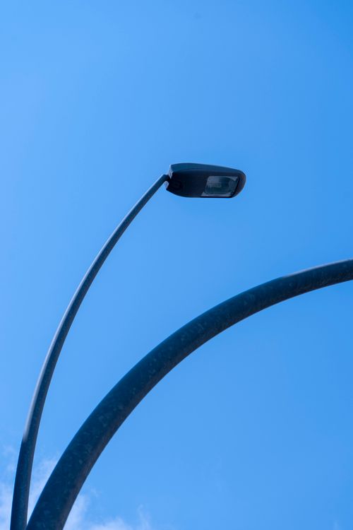 Free Modern street lamp curves elegantly against a vivid blue sky, capturing urban minimalism. Stock Photo