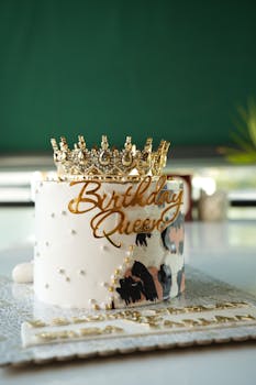 A luxurious white birthday cake adorned with a gold crown and decorative pearls, perfect for celebrations.