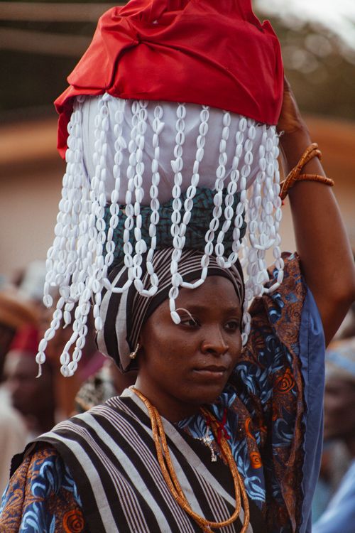 Free A woman in traditional attire carrying ornate headwear during an outdoor African cultural ceremony. Stock Photo