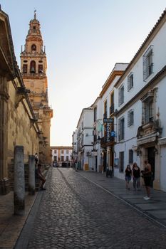 A charming view of a historic street in Córdoba, Spain featuring the Mosque-Cathedral at sunset.