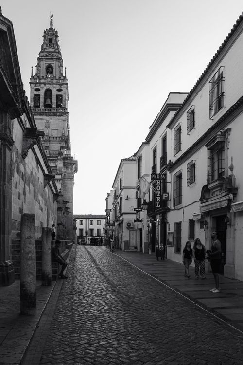 Free Black and white street view of Córdoba, Spain featuring historic architecture and a bell tower. Stock Photo