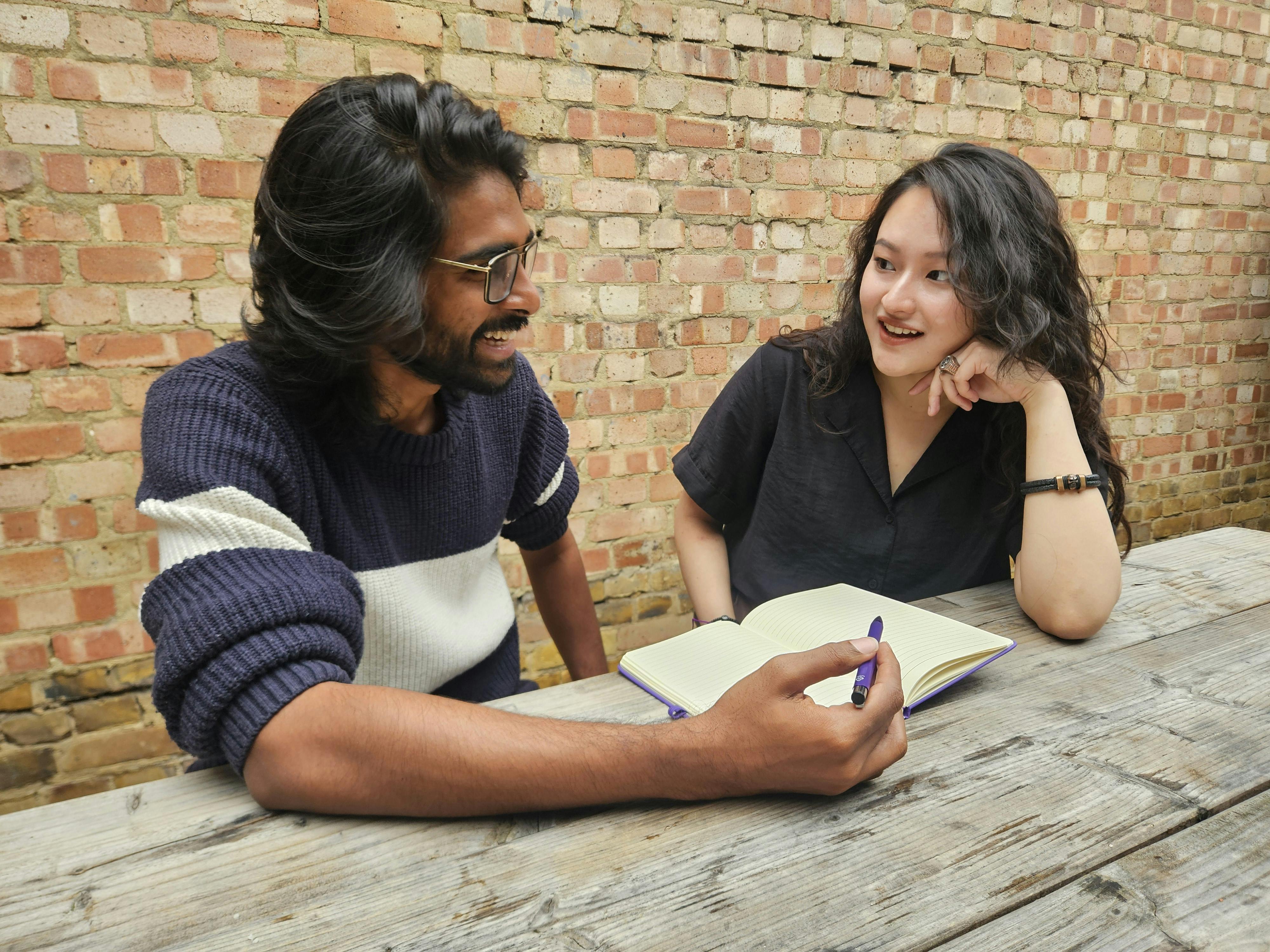 Due giovani adulti che discutono e prendono appunti durante una conversazione all'aperto