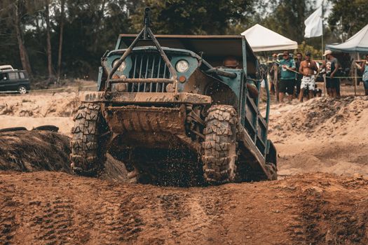 A rugged off-road vehicle powers through a muddy track as onlookers watch the thrilling outdoor event.