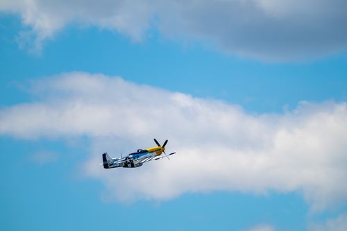 Free A P-51 Mustang aircraft soaring through a bright blue sky with scattered clouds. Stock Photo