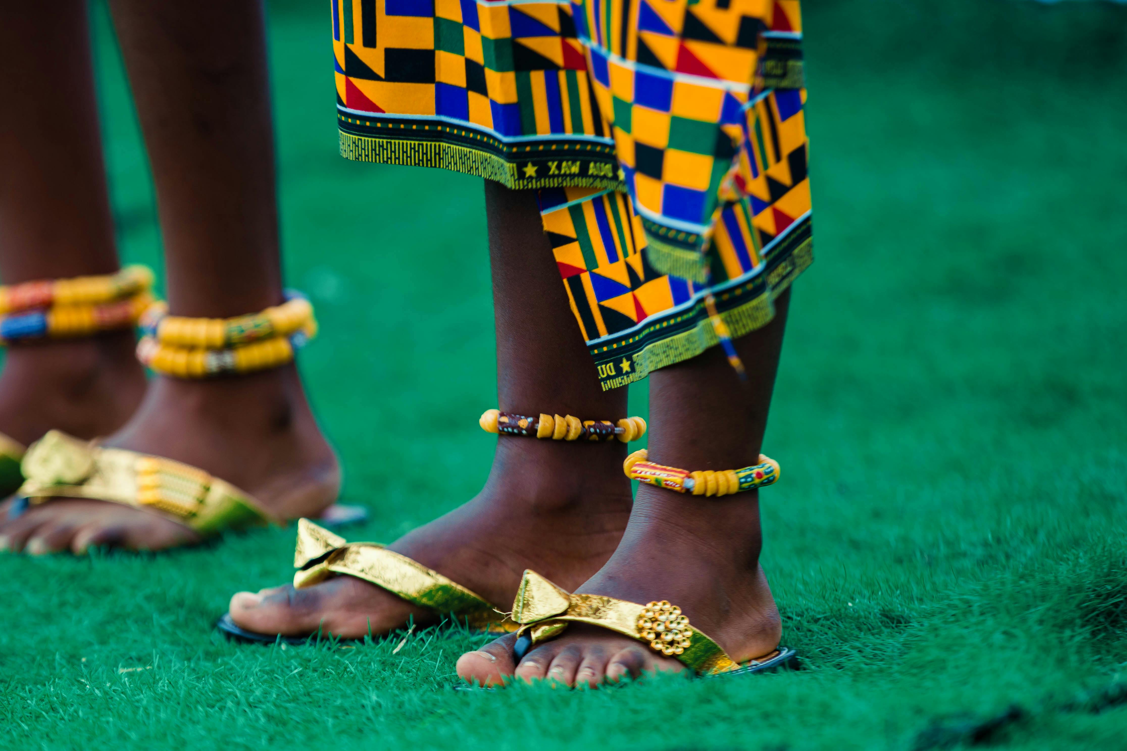 Vibrant Kente patterns and bead jewelry adorn feet for a cultural celebration in Ghana.