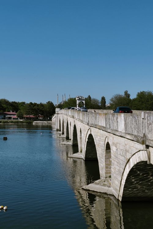 Free A stone bridge spans a tranquil river under a clear blue sky, evoking historical charm and serenity. Stock Photo
