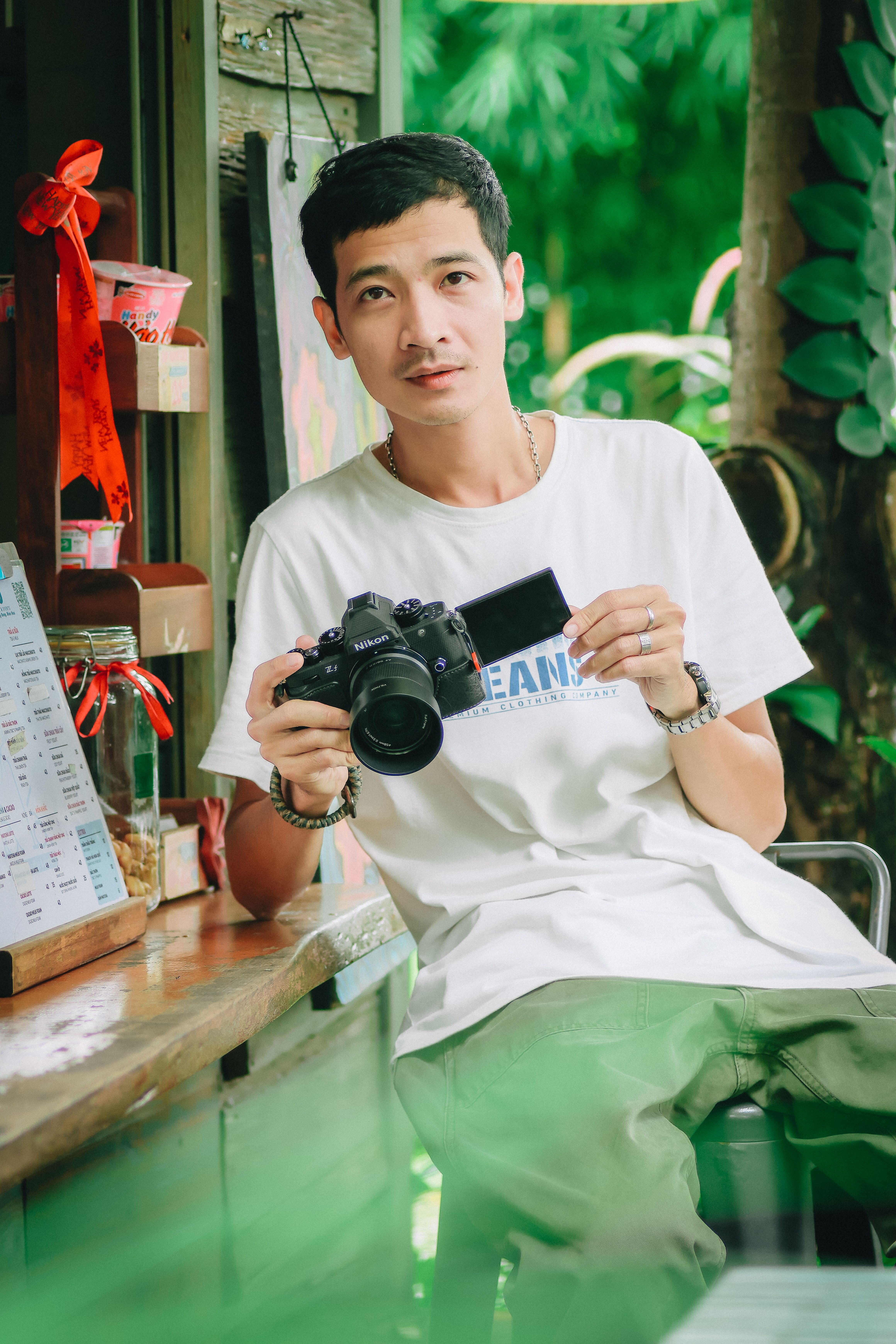 Young photographer posing with camera in a cozy outdoor café setting, exuding a casual and relaxed vibe.