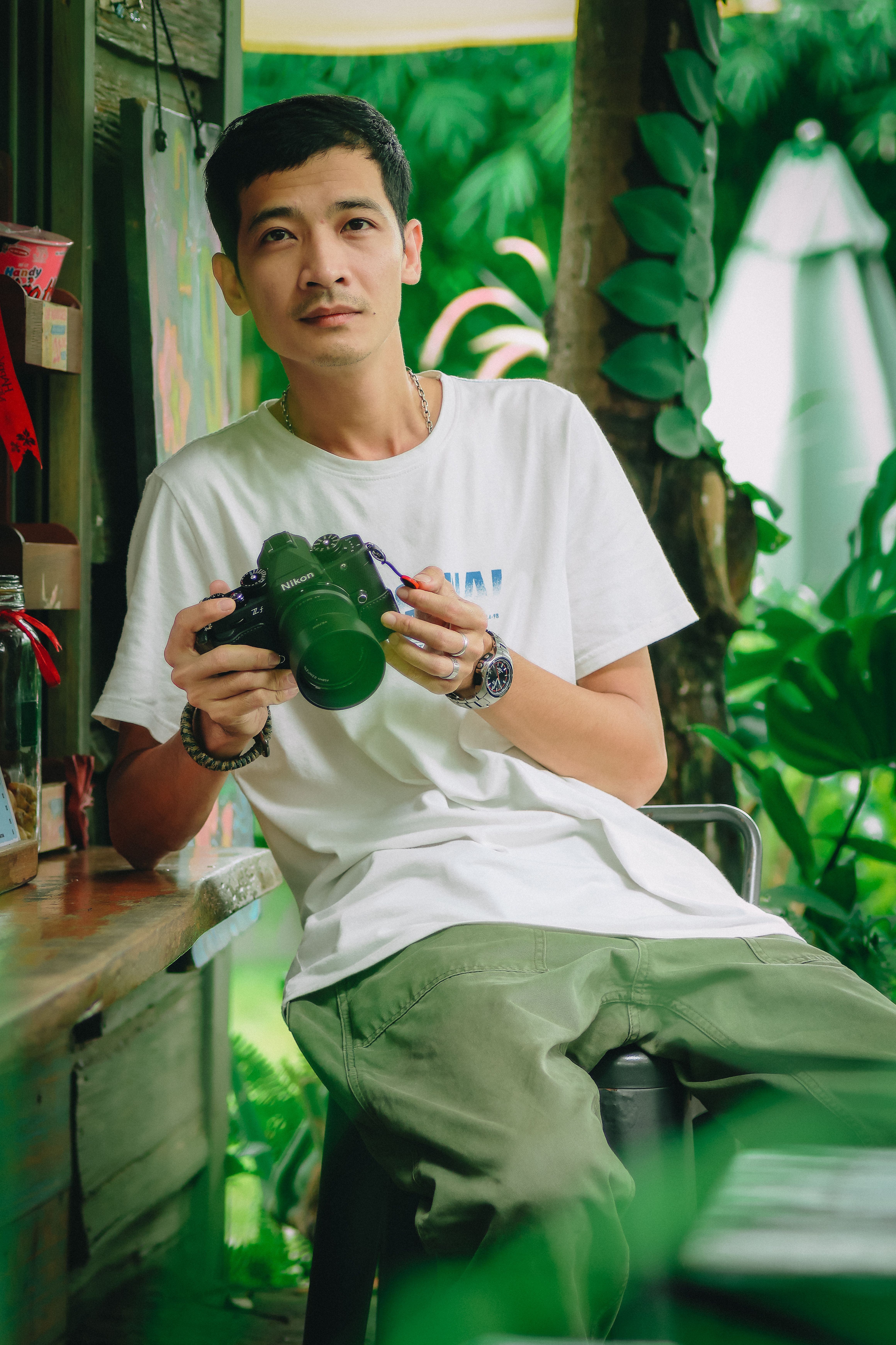 Man holding camera in lush tropical setting, relaxed vibe.