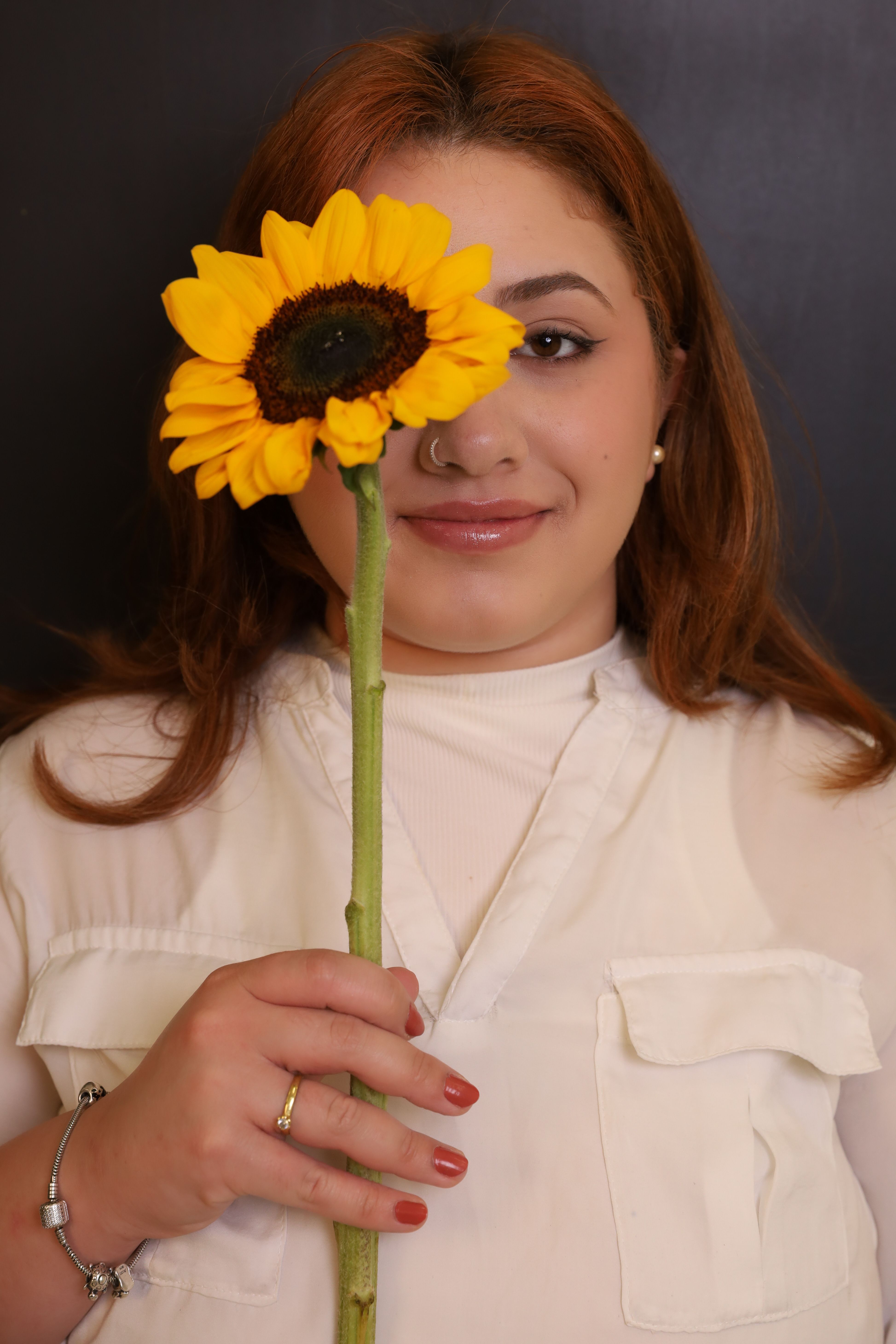 A woman smiling while holding a sunflower against a black background indoors.