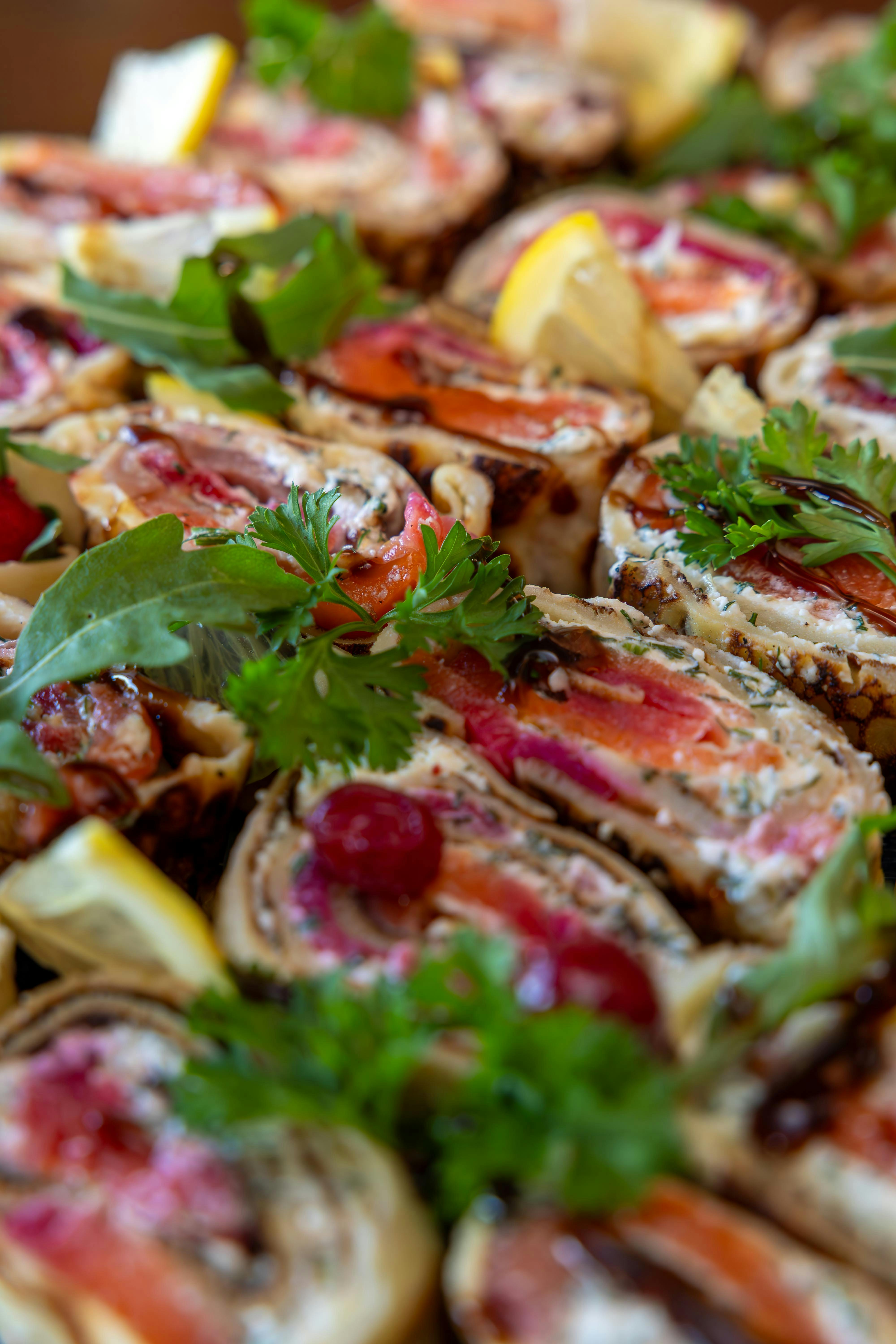 Close-up of colorful stuffed crepes garnished with fresh herbs and lemon wedges.