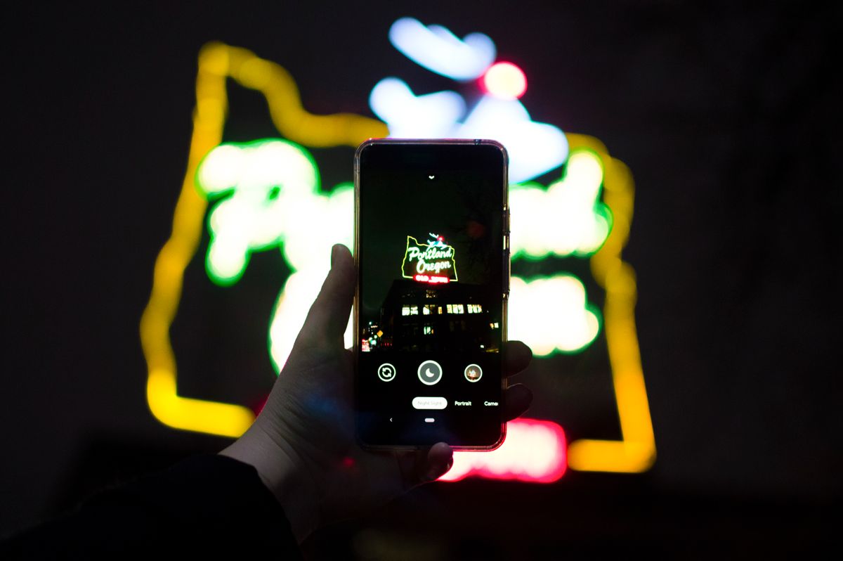 Um celular fotografando uma placa iluminada à noite